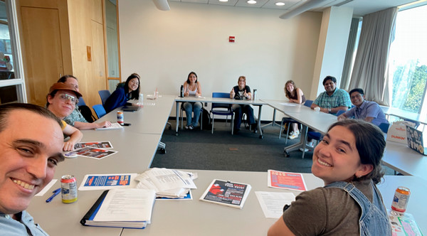 students and staff sitting at square table in a Brandies meeting room smiling